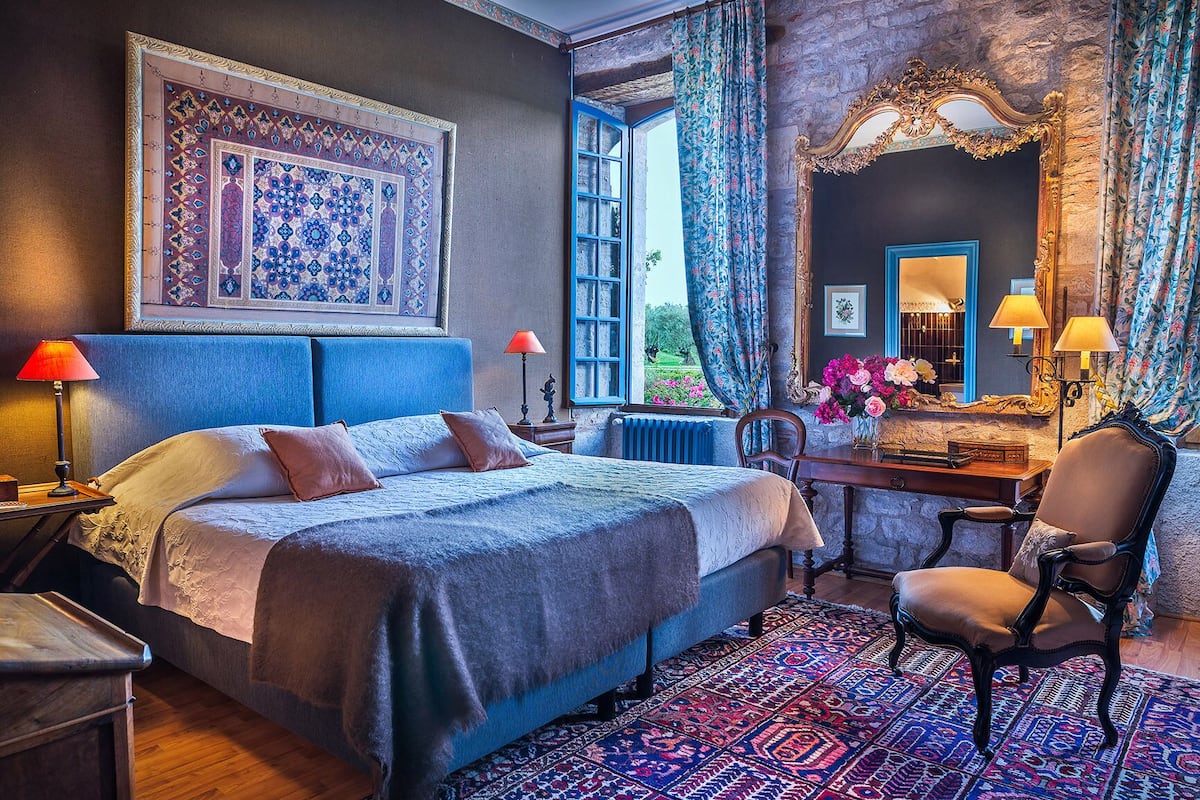 Une chambre avec un grand lit, un bureau avec une lampe, une chaise et un grand miroir.