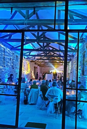 Evento interior con escenario y público sentado en mesas, bajo un techo con estructura de madera.
