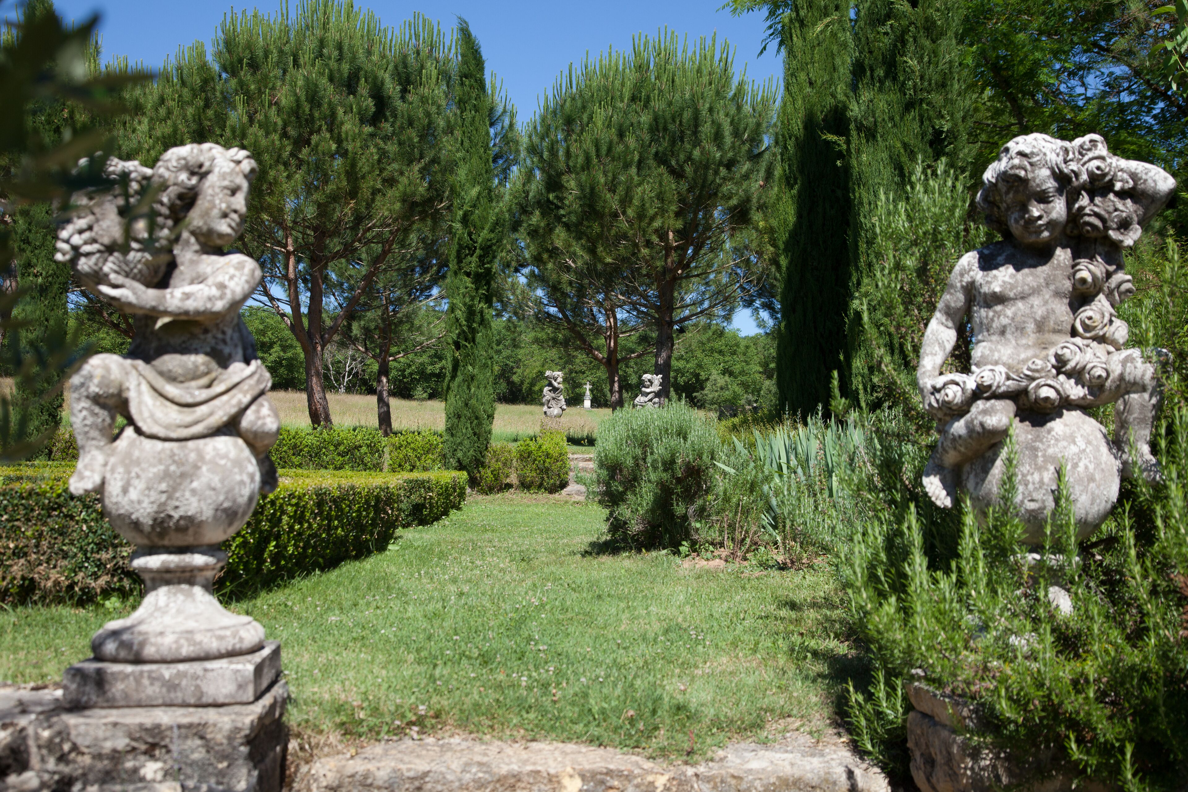 A garden with statues and neatly trimmed hedges.