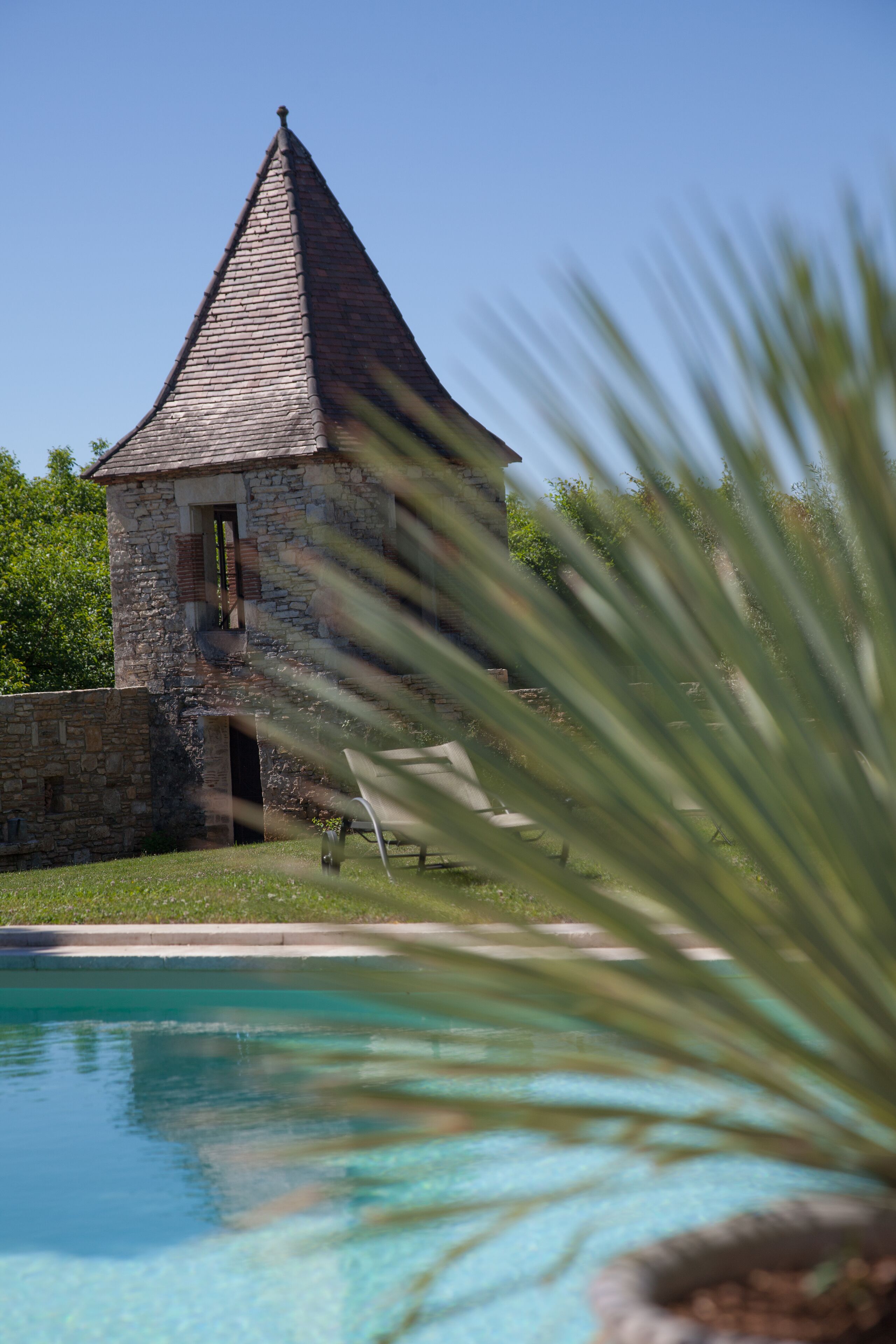 A stone building with a conical roof near a swimming pool.