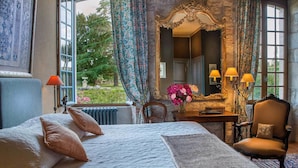 A bedroom with a large bed, a desk with a mirror, and a view of greenery outside. - Domaine de Labarthe (Espere)