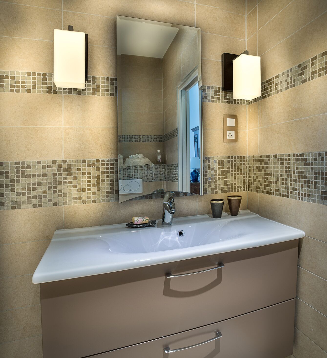 A bathroom with a large mirror, a sink, and two wall-mounted lights.