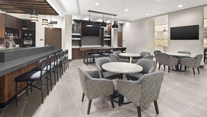 A modern bar area with a counter, bar stools, and a television screen. There are round tables with chairs in the dining area.