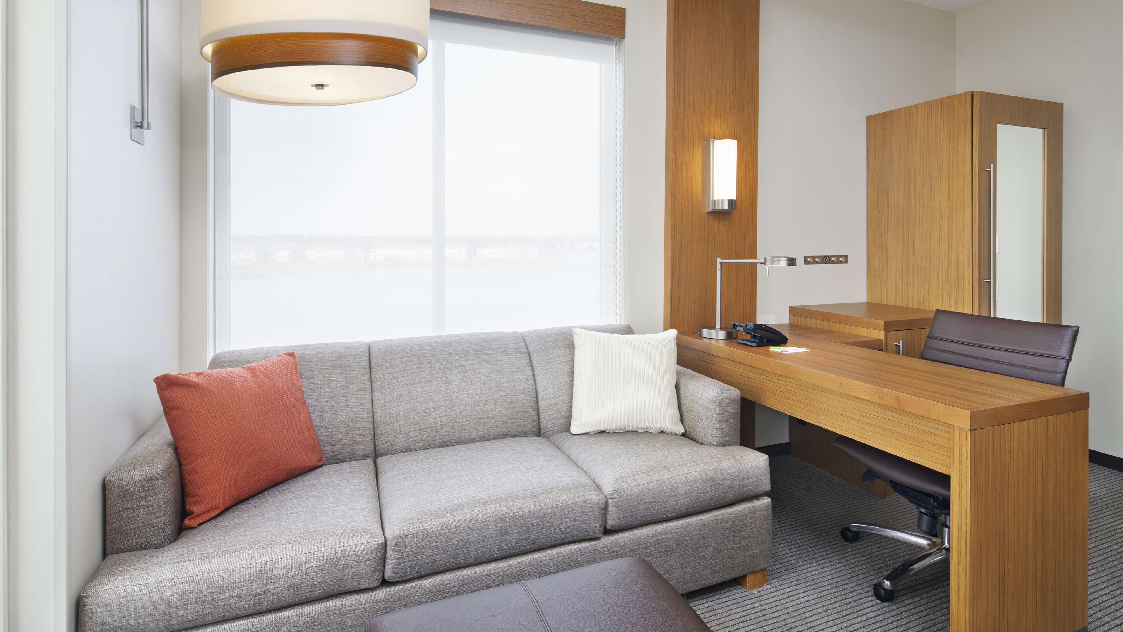 A modern hotel room with a grey sofa, a wooden desk, a laptop, and a desk lamp.