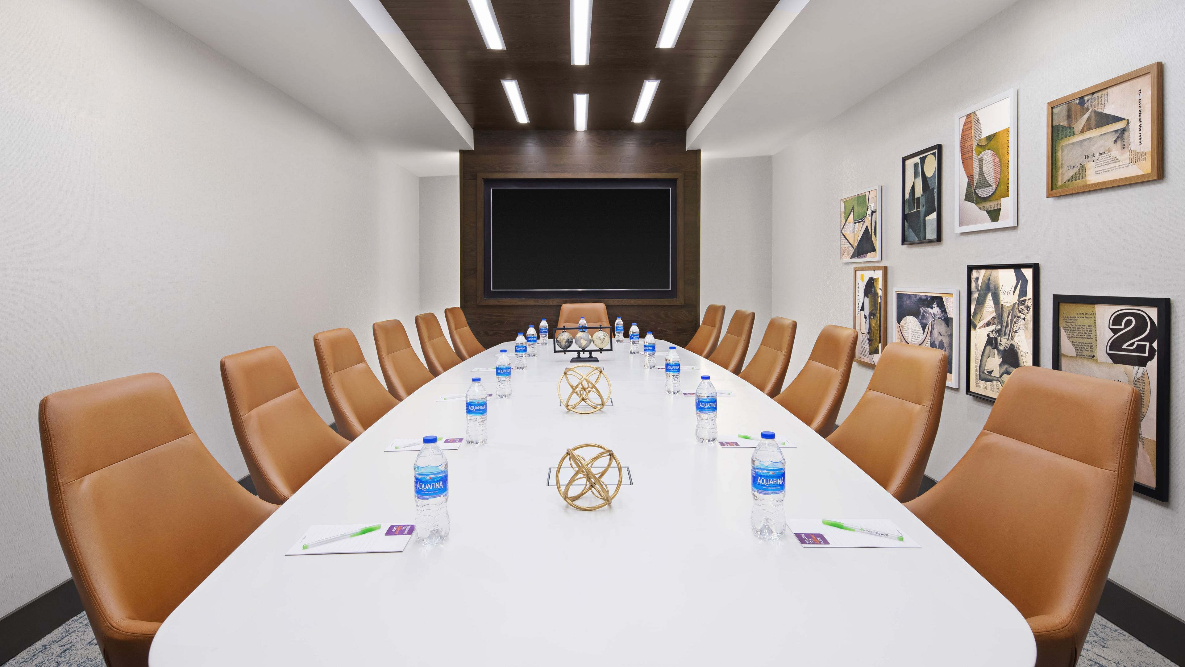 A conference room with a long table, brown leather chairs, water bottles, and framed artwork on the walls.