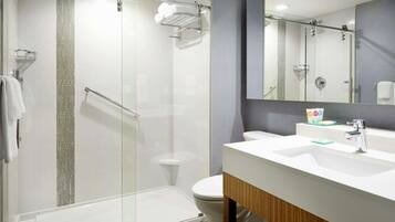 Un baño moderno con ducha de vidrio, inodoro blanco y tocador con espejo.