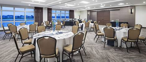 A conference room with round tables, beige chairs, and large windows offering a view of the sea.