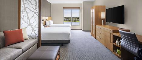 Quarto de hotel com cama, sofá, escrivaninha, cadeira e televisão.