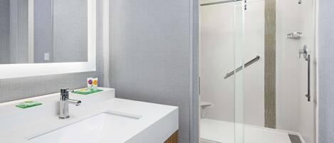 Un baño moderno con un espejo grande, lavamanos blanco y cabina de ducha con mampara de vidrio.