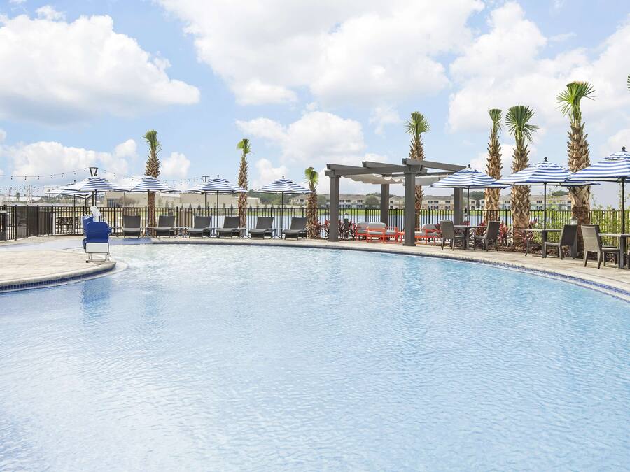 A swimming pool with lounge chairs and umbrellas, surrounded by palm trees and a fence.
