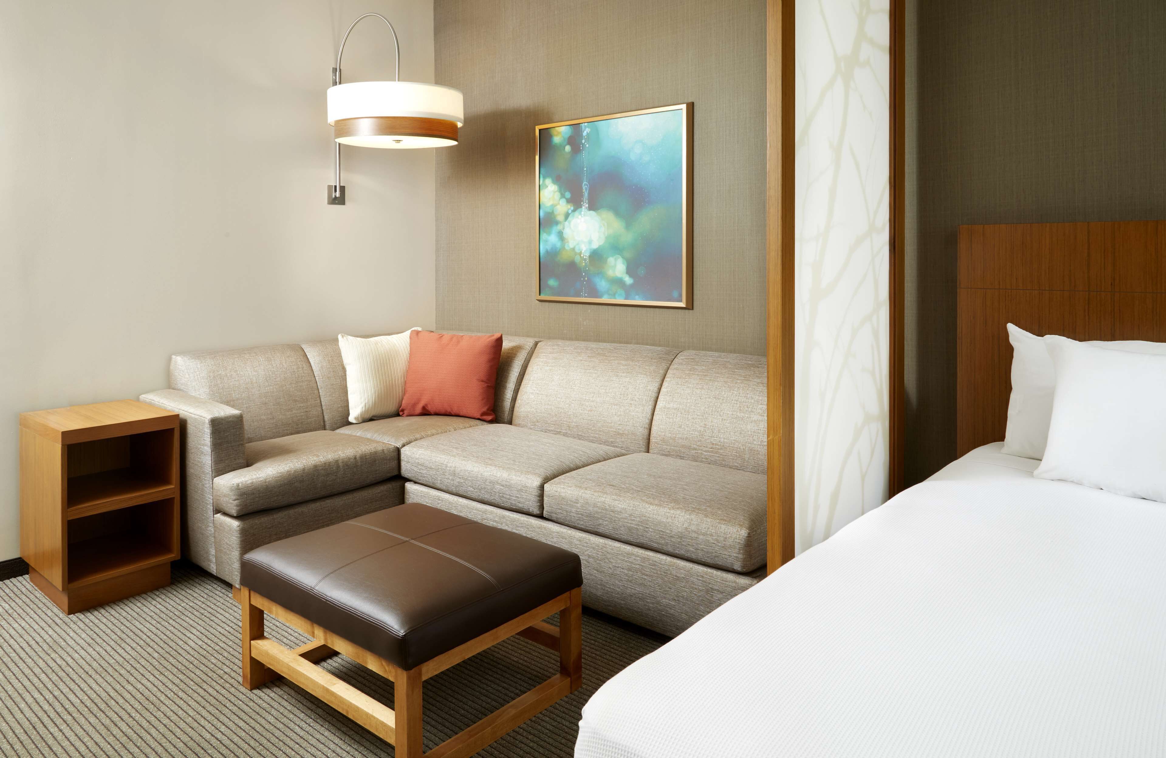 Habitación de hotel con sofá, mesita de madera, banco, cama y lámpara de pared.