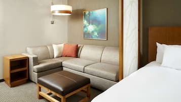 Habitación de hotel con sofá, mesita de madera, banco, cama y lámpara de pared.