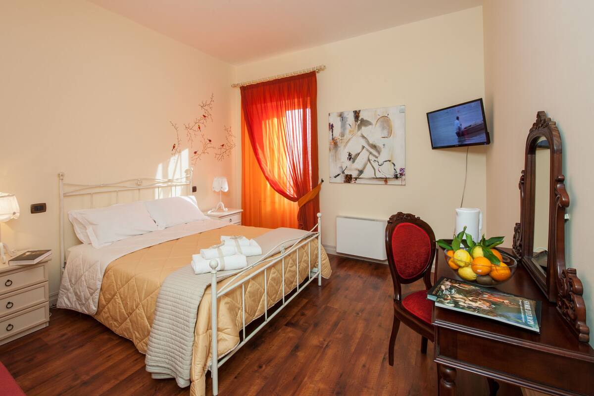 Habitación de hotel con cama, mesitas de noche, escritorio con espejo, una silla y televisor.