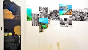 Une pièce avec une porte blanche, une fenêtre ornée d’un rideau décoratif et un mur où sont accrochées plusieurs photographies encadrées.
