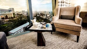 A modern hotel room with a large window offering a city view, a comfortable armchair, a small table with a tea set, and a carpeted floor. - Apartments by Fairmont Baku Flame Towers (Baku)