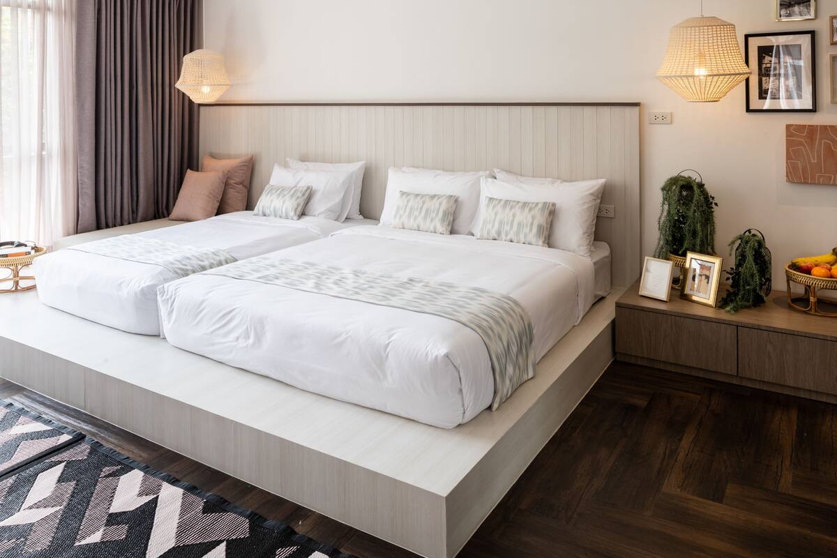 A modern hotel room with a large bed, a bedside table with a lamp, a small plant, and a fruit basket.