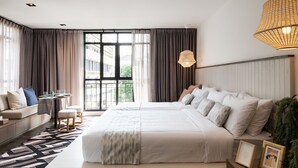 A modern hotel room with a large bed, a sofa, a dining table, and a view of the city.