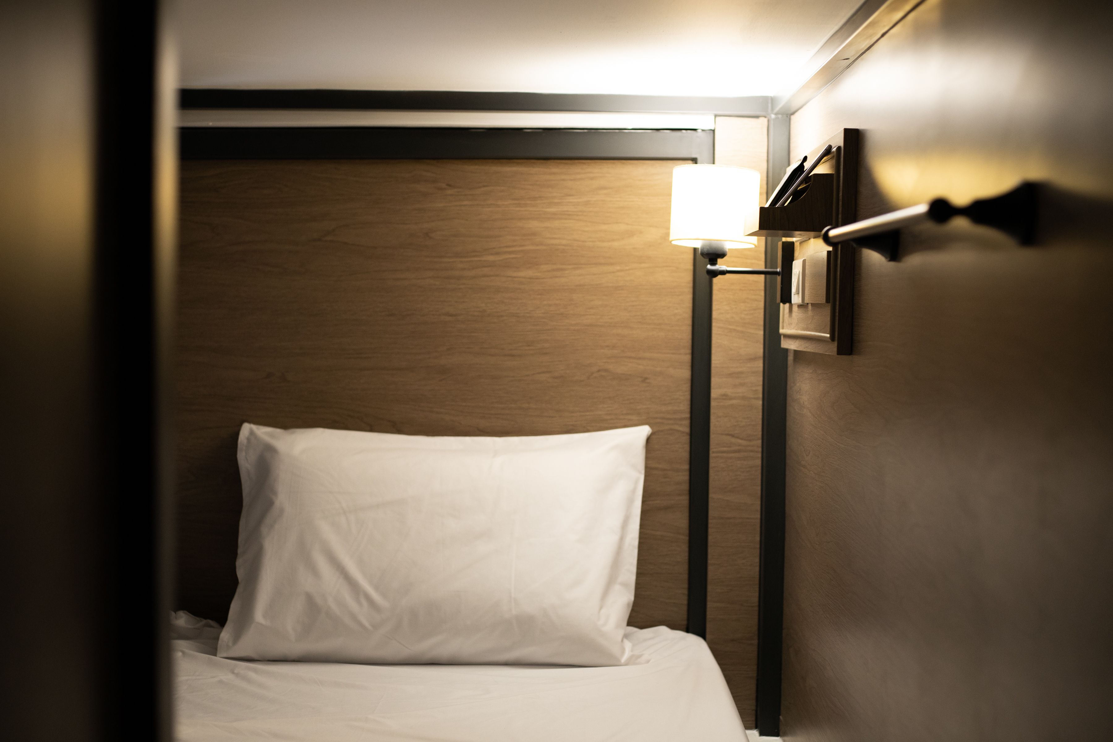 A hotel room with a neatly made bed, a bedside lamp, and a wooden headboard.
