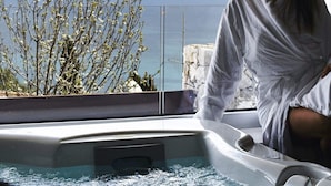 A person in a white robe sitting in a hot tub with a view of the ocean and a tree in the background. - The View luxury apartments Taormina (Taormina)