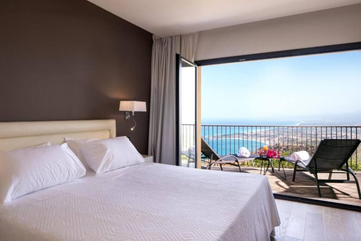 Een hotelkamer met een groot bed, een balkon met uitzicht op zee en twee stoelen.