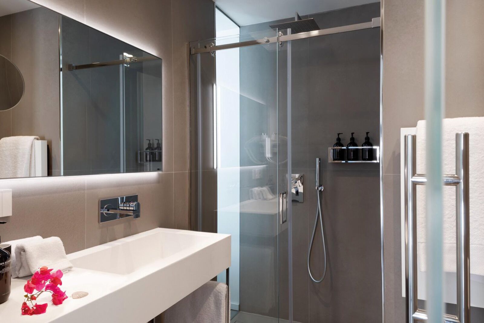A modern bathroom with a glass-enclosed shower, a white sink with a mirror above, and a towel rack.