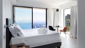 A modern hotel room with a large bed, a TV, a balcony with a table and chairs, and a view of the ocean. - The View luxury apartments Taormina (Taormina)