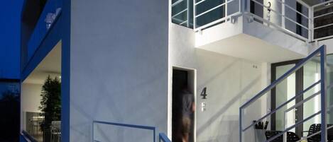 A modern building with a glass entrance, a balcony, and a dining area with chairs.