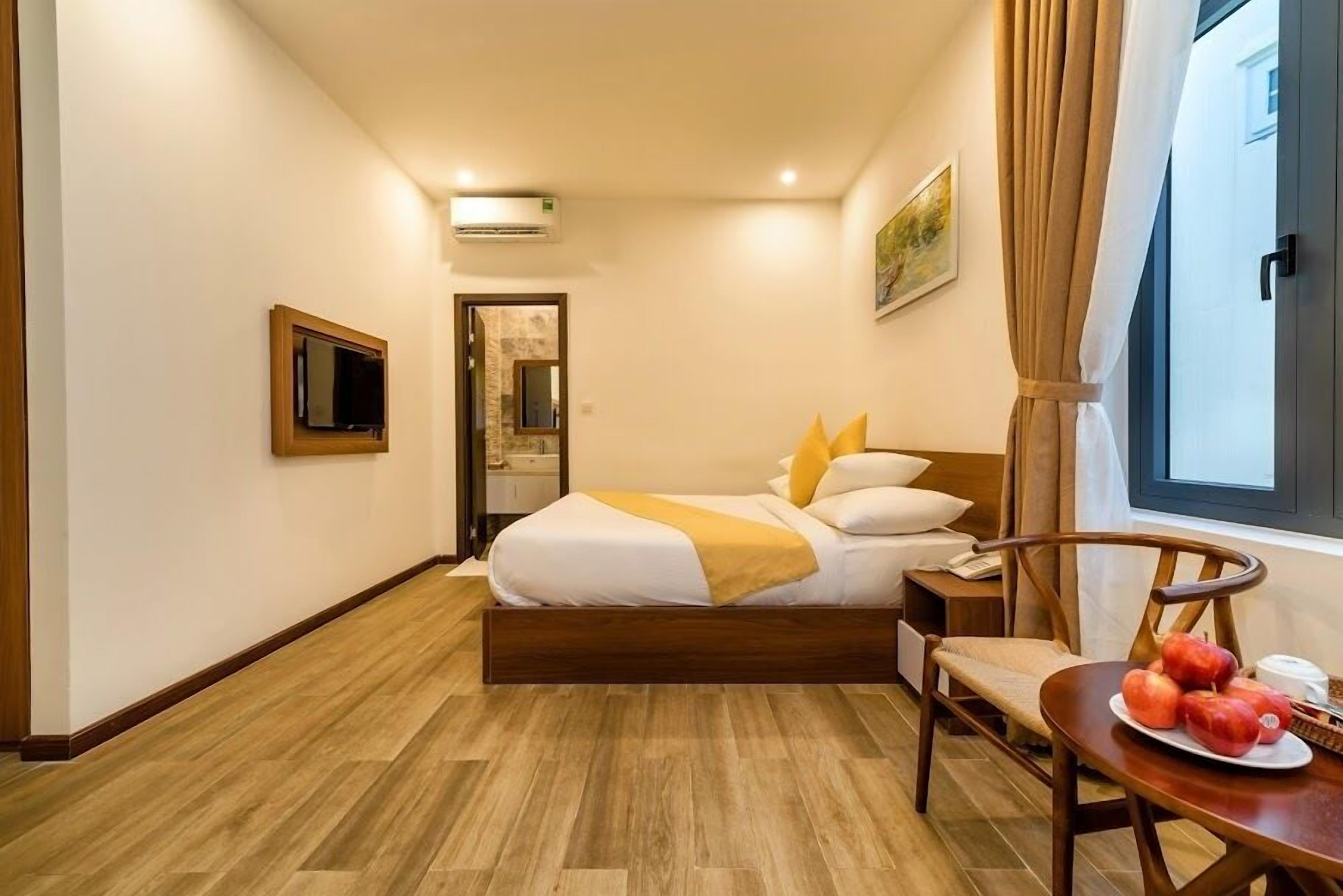 A hotel room with a bed, a chair, a table with fruit, and a painting on the wall.