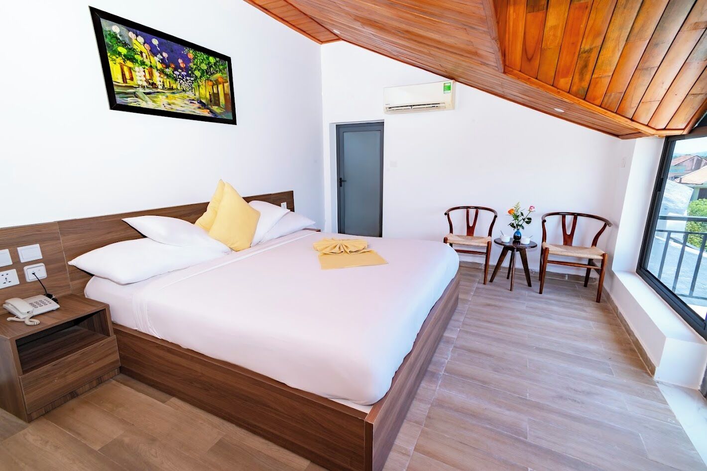 A hotel room with a bed, bedside table, and a painting on the wall.