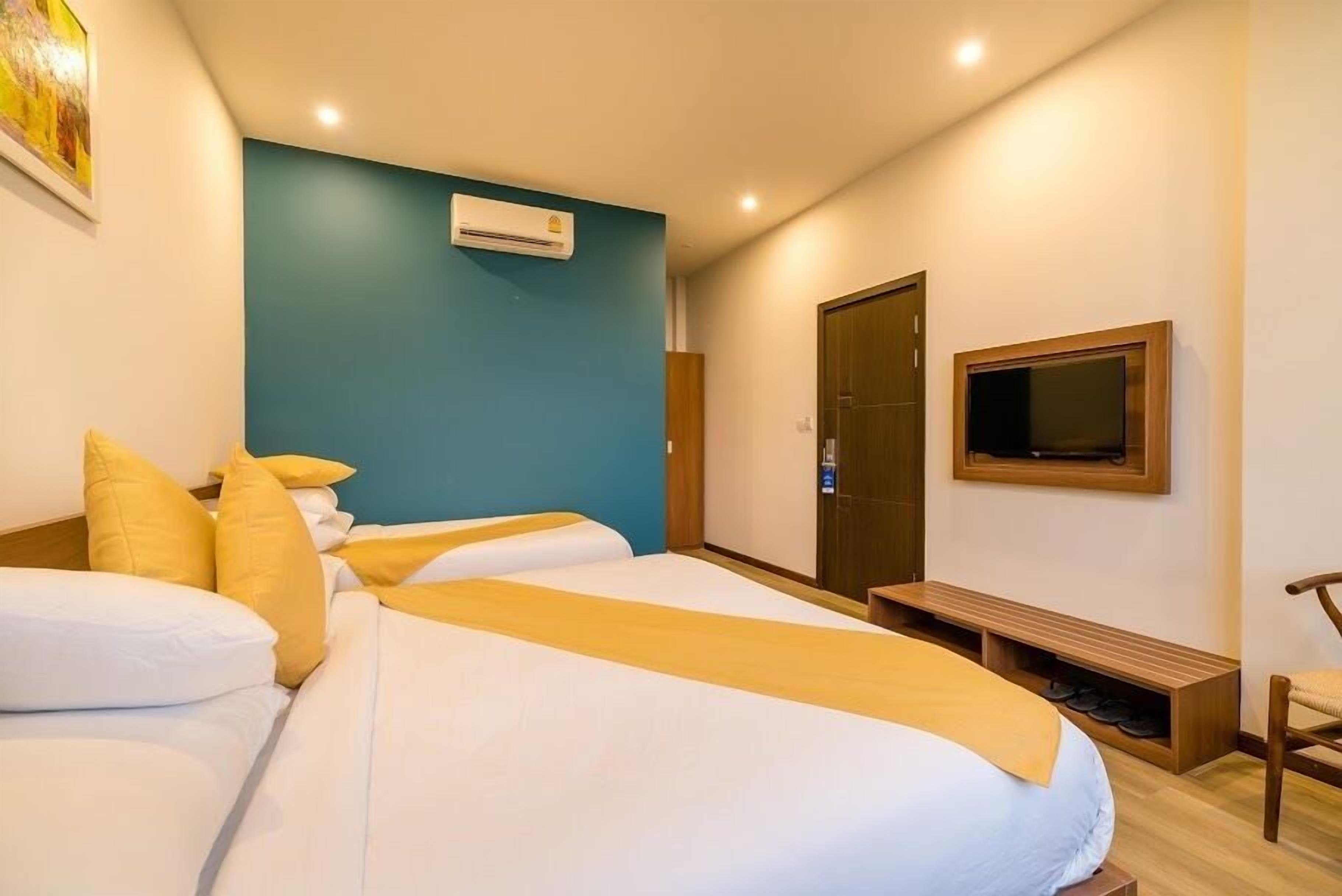 A hotel room with two beds, a TV, a wardrobe, and a bench.