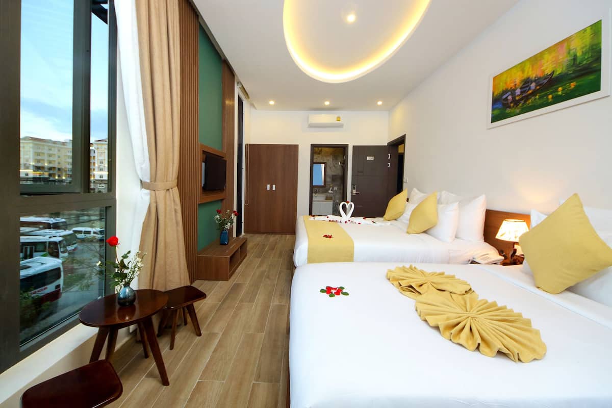 Ein Hotelzimmer mit zwei Betten, einem Fenster mit Blick auf Stadtgebäude, einem kleinen Tisch mit einer Vase und einem Gemälde an der Wand.