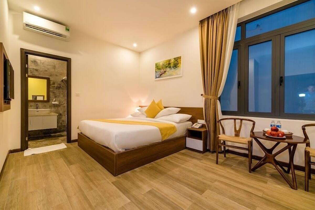 Ein Hotelzimmer mit Bett, Nachttisch, Sessel und einem Fenster mit Vorhängen.