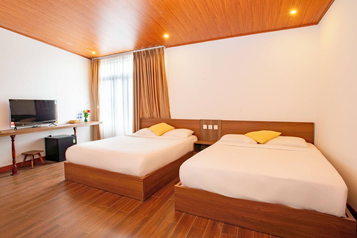 Ein Hotelzimmer mit zwei Holzbetten, einem Schreibtisch mit Fernseher und einem kleinen Hocker.