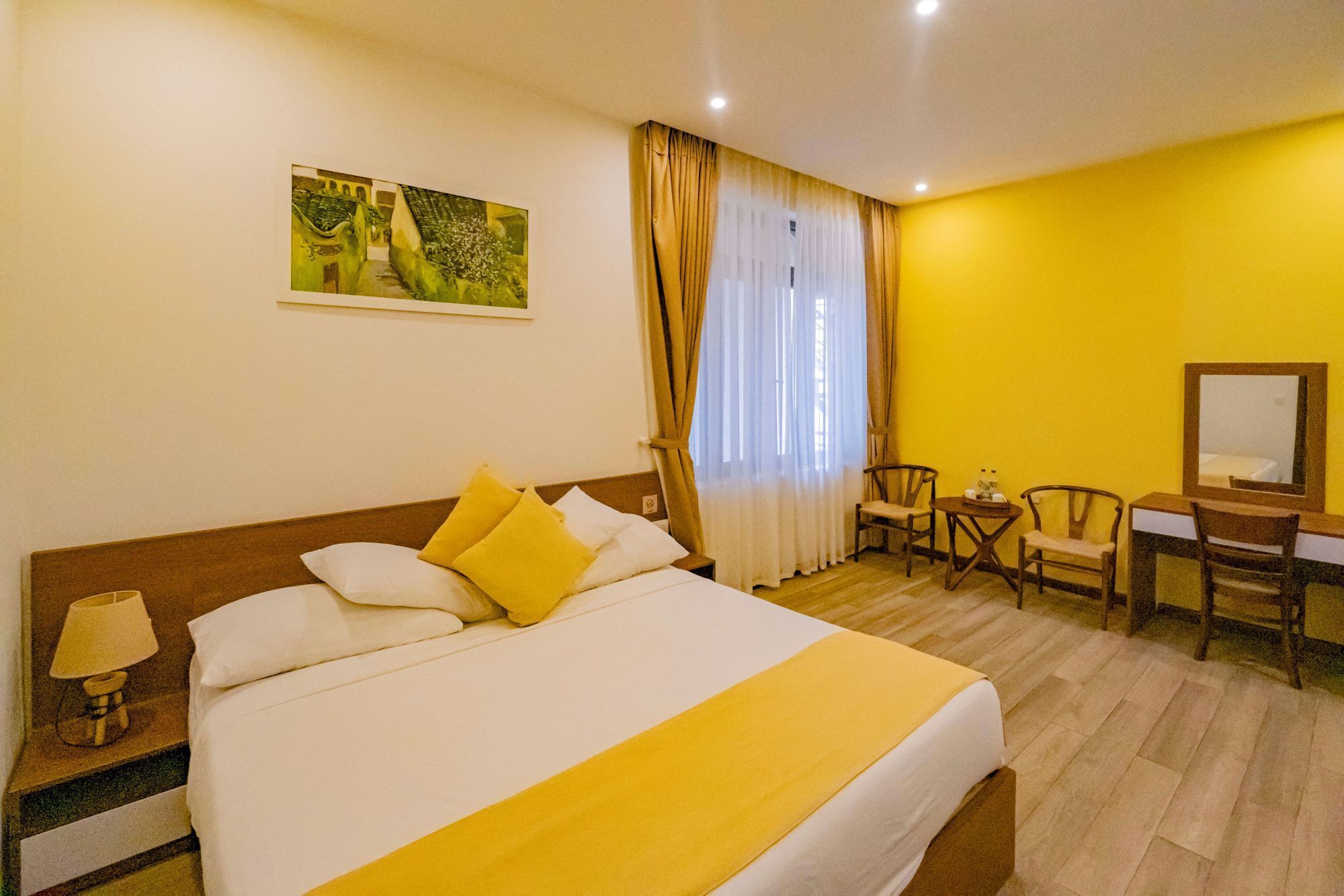 A hotel room with a large bed, a desk with chairs, a small table, and a painting on the wall.