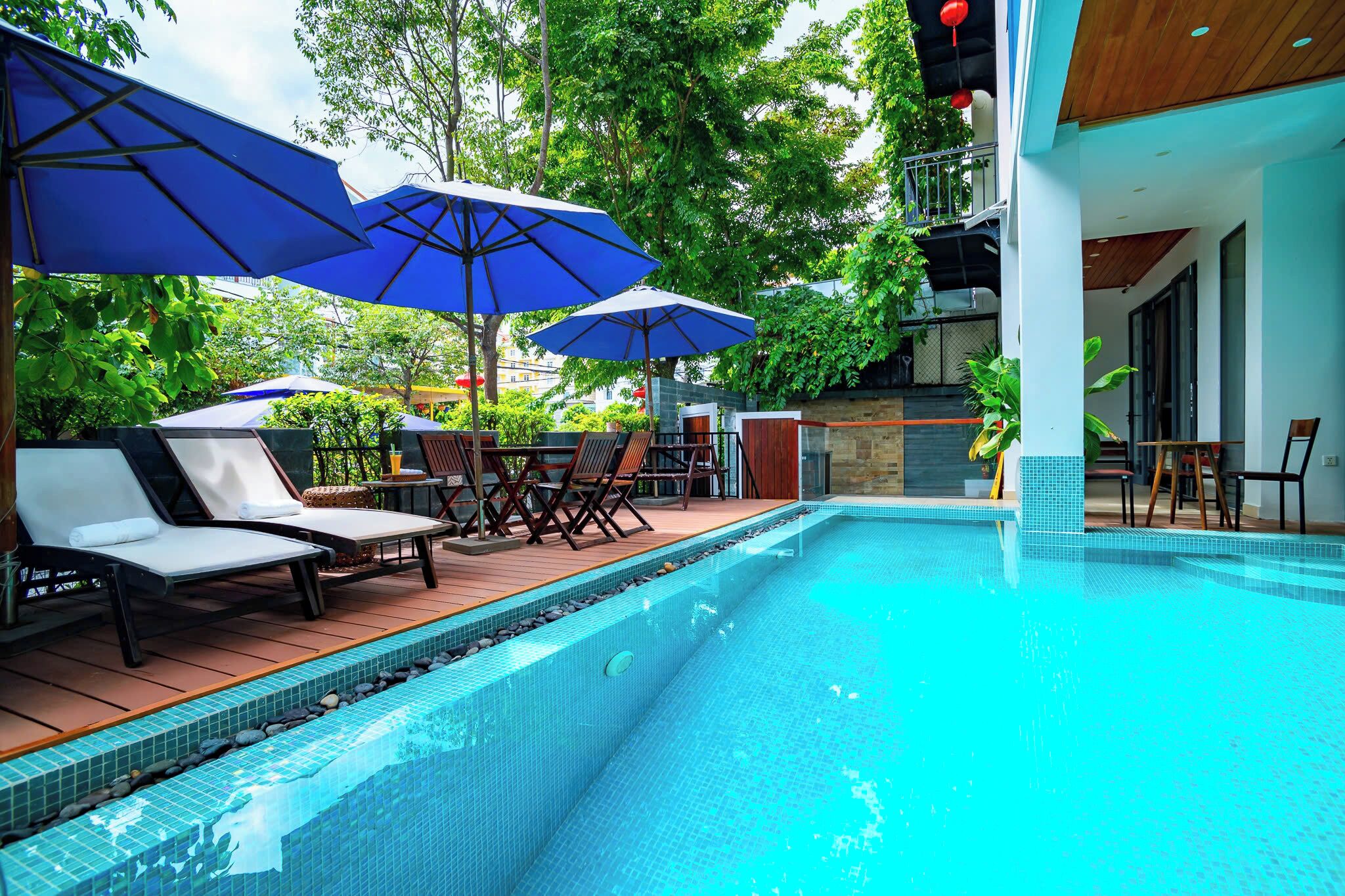 A poolside area with lounge chairs and umbrellas, surrounded by greenery.