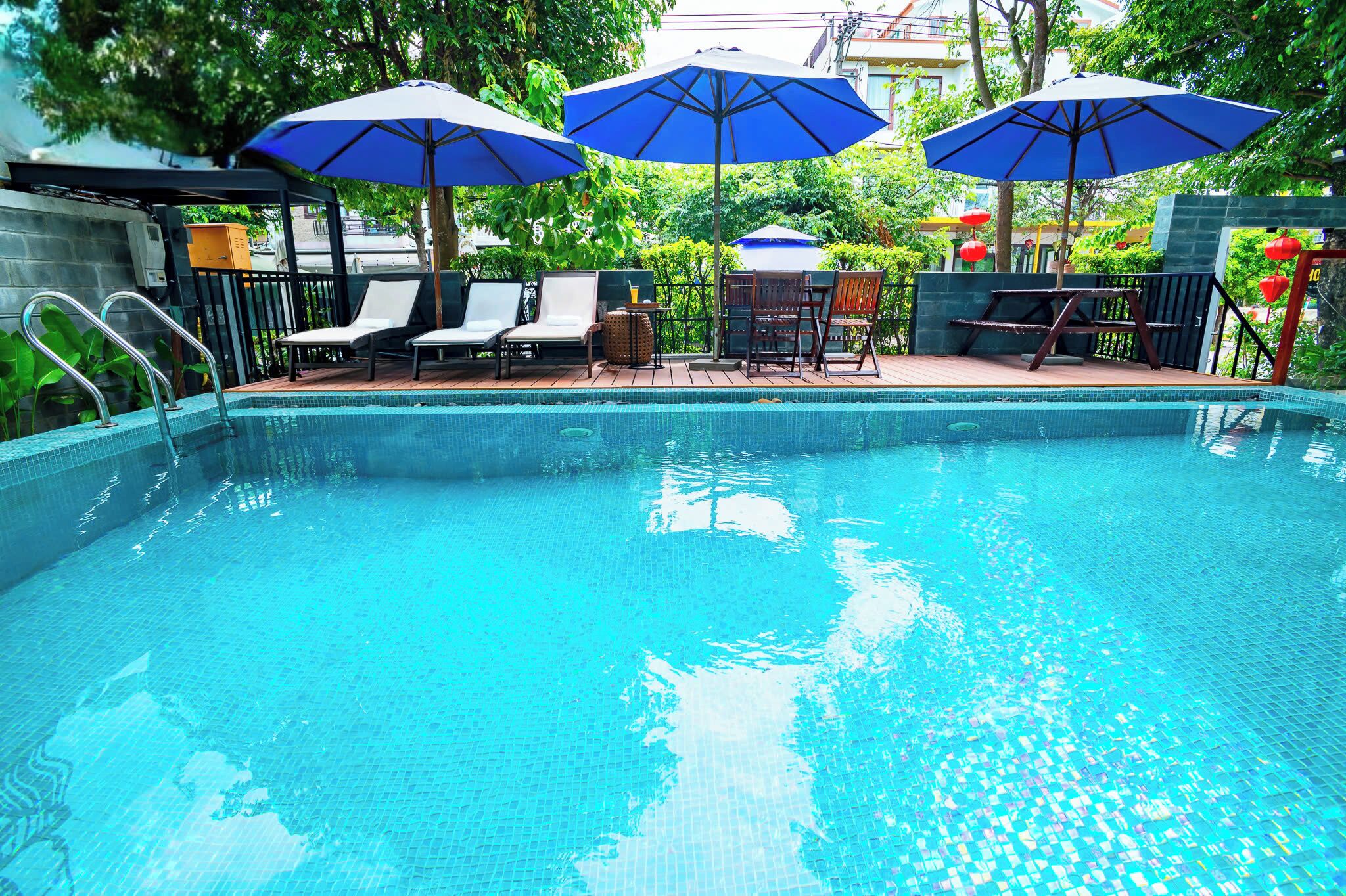 A swimming pool with lounge chairs and umbrellas, surrounded by greenery.
