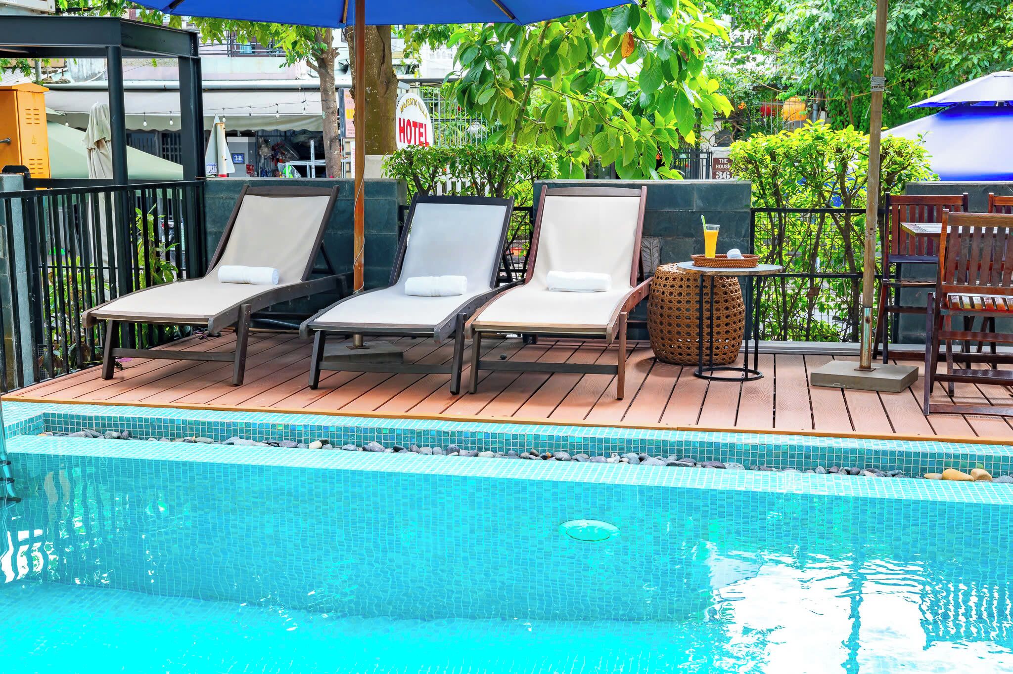 A poolside area with lounge chairs, a small table with a drink, and a sign for a hotel in the background.