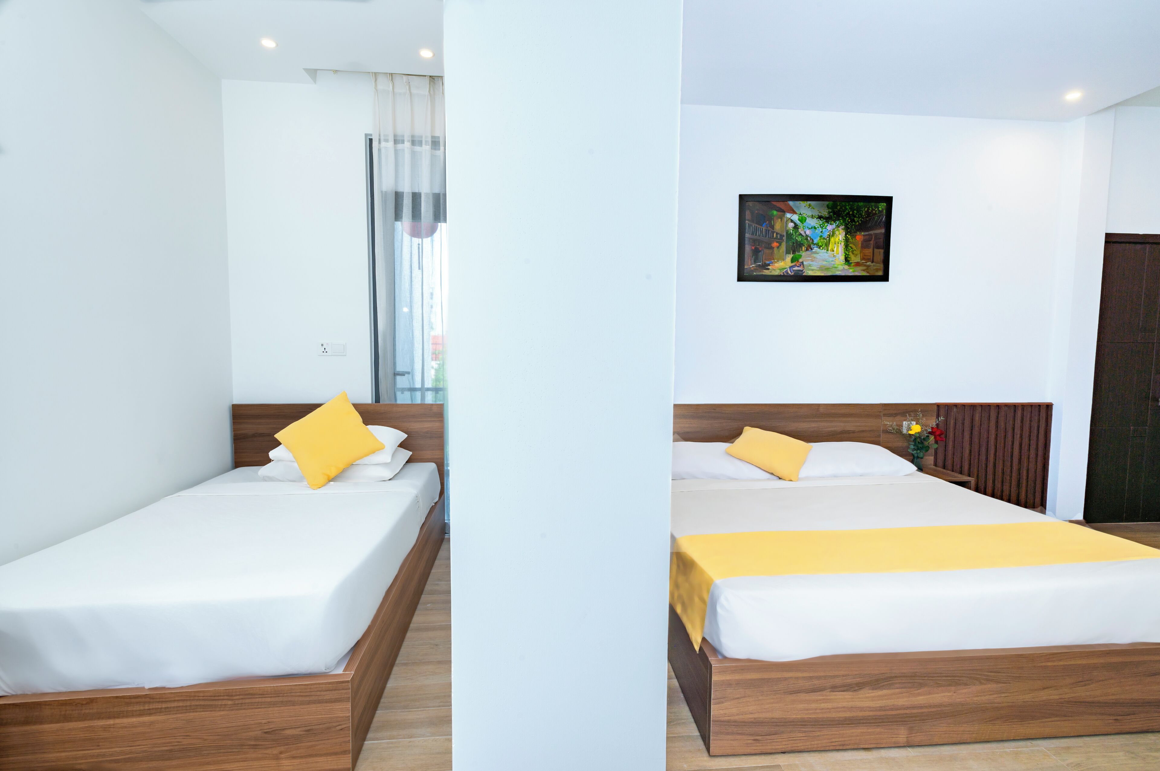 A hotel room with a single bed, a window with curtains, a painting on the wall, and a wooden headboard.