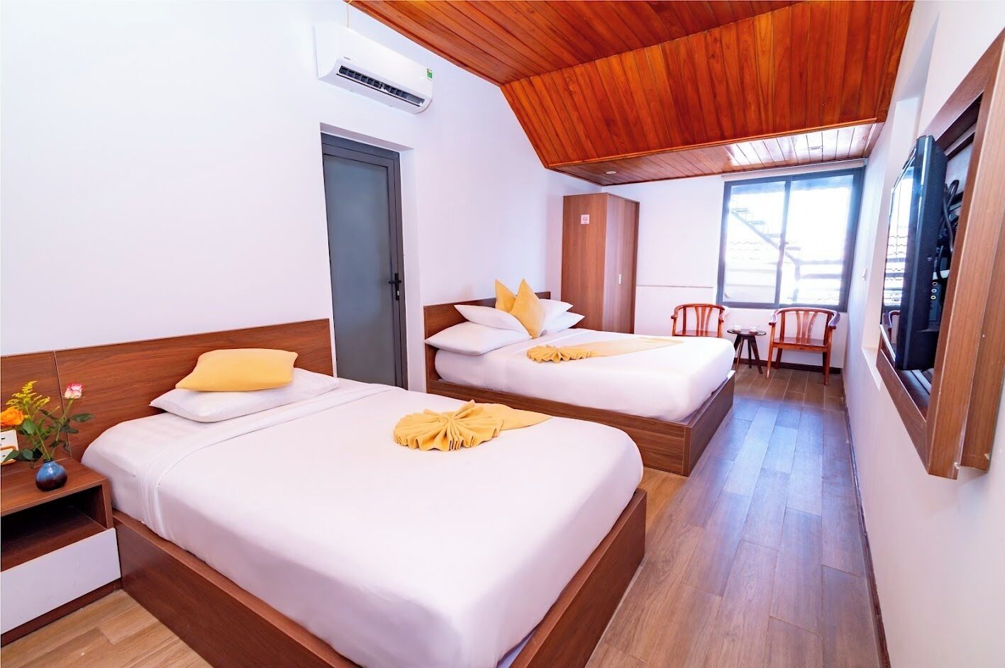 A hotel room with two beds, wooden ceiling, and a view of the outside.