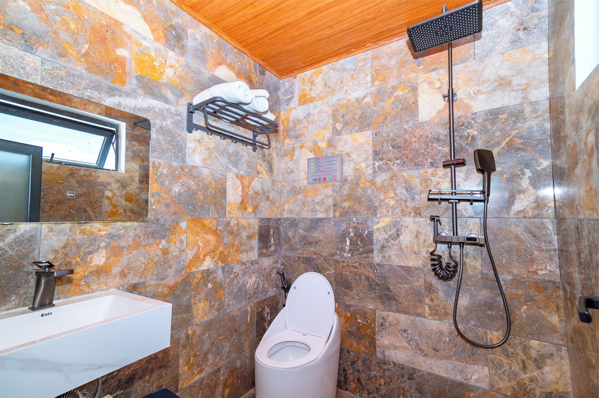 Een moderne badkamer met een marmeren wand, een witte wastafel, toilet en douche.
