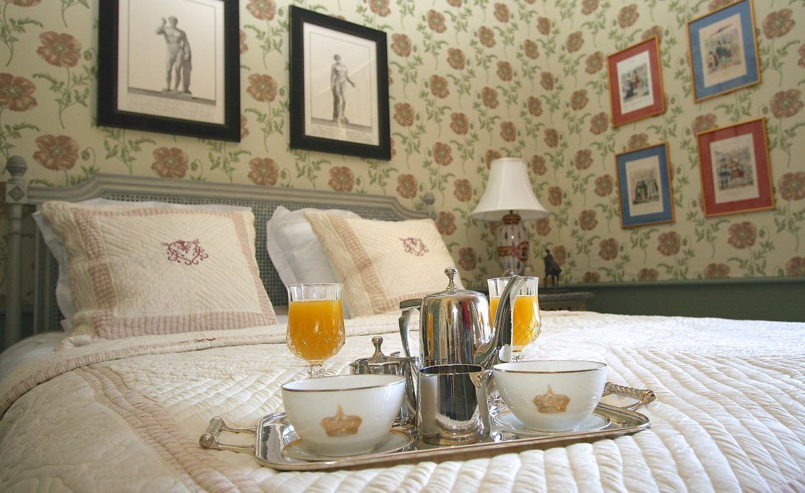 A neatly made bed with a tray of breakfast items including a teapot, cups, and glasses of orange juice.