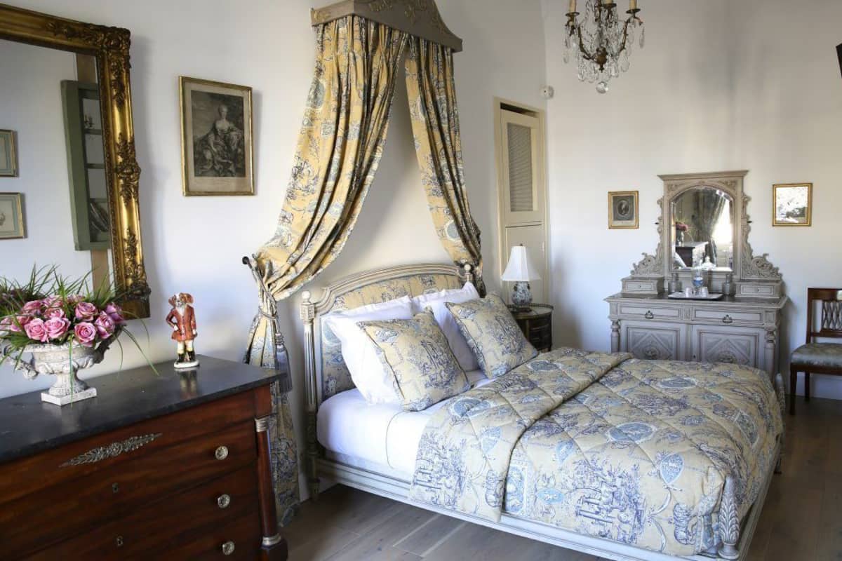 A bedroom with a four-poster bed, a dresser, a vanity with a mirror, and a chandelier.