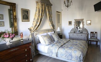 Un dormitorio con una cama con dosel, un aparador, un tocador con espejo y una araña.