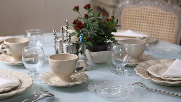 Una mesa dispuesta con vajilla de porcelana, cubiertos y una planta en maceta con flores rojas.