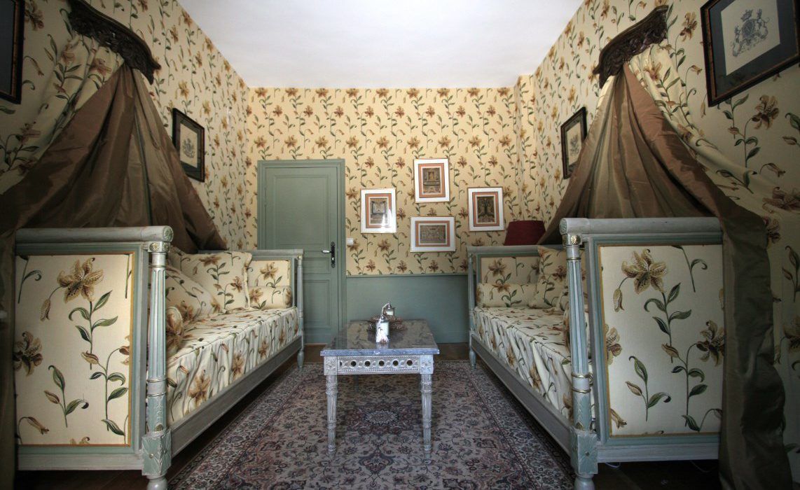 A room with two beds, a small table, and floral wallpaper.