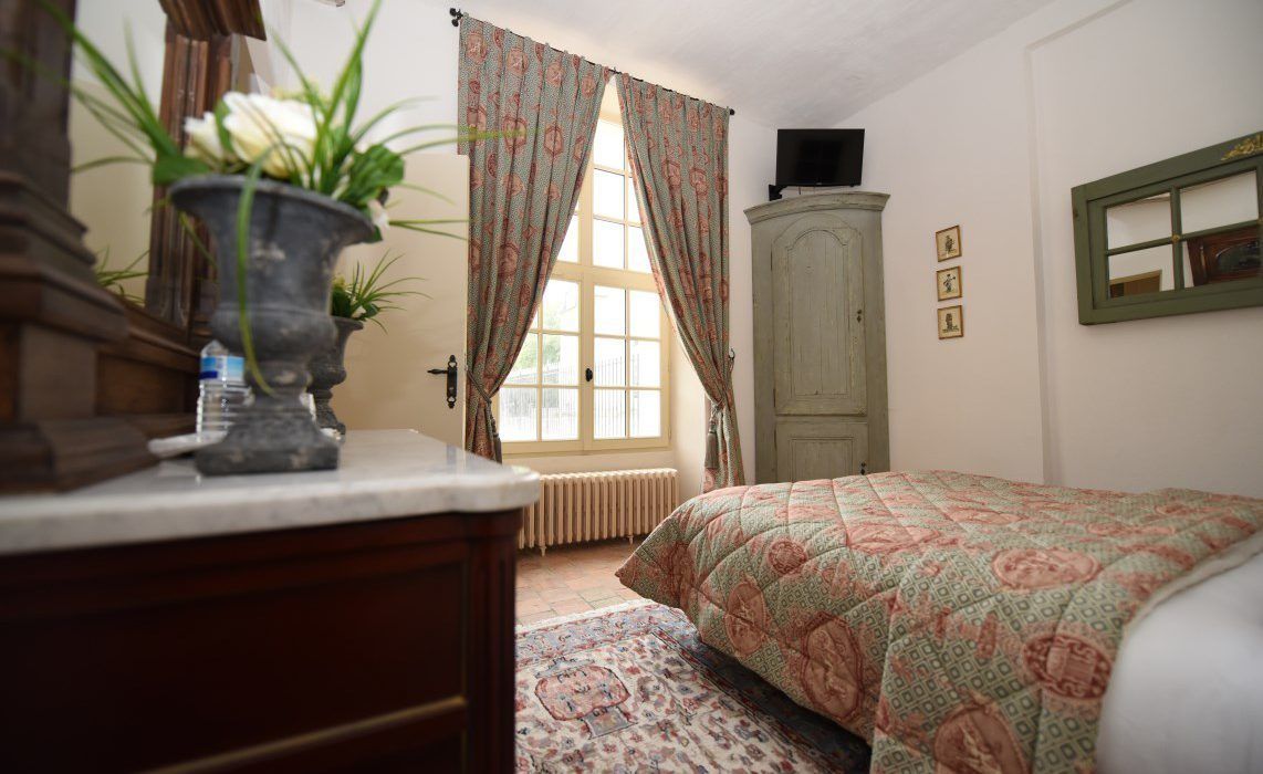 Un dormitorio con cama, cómoda, radiador, ventana con cortinas, armario y televisor.