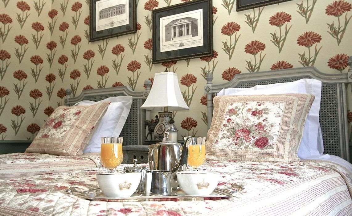 A neatly made bed with a tray of breakfast items, including a teapot, cups, and glasses of orange juice.