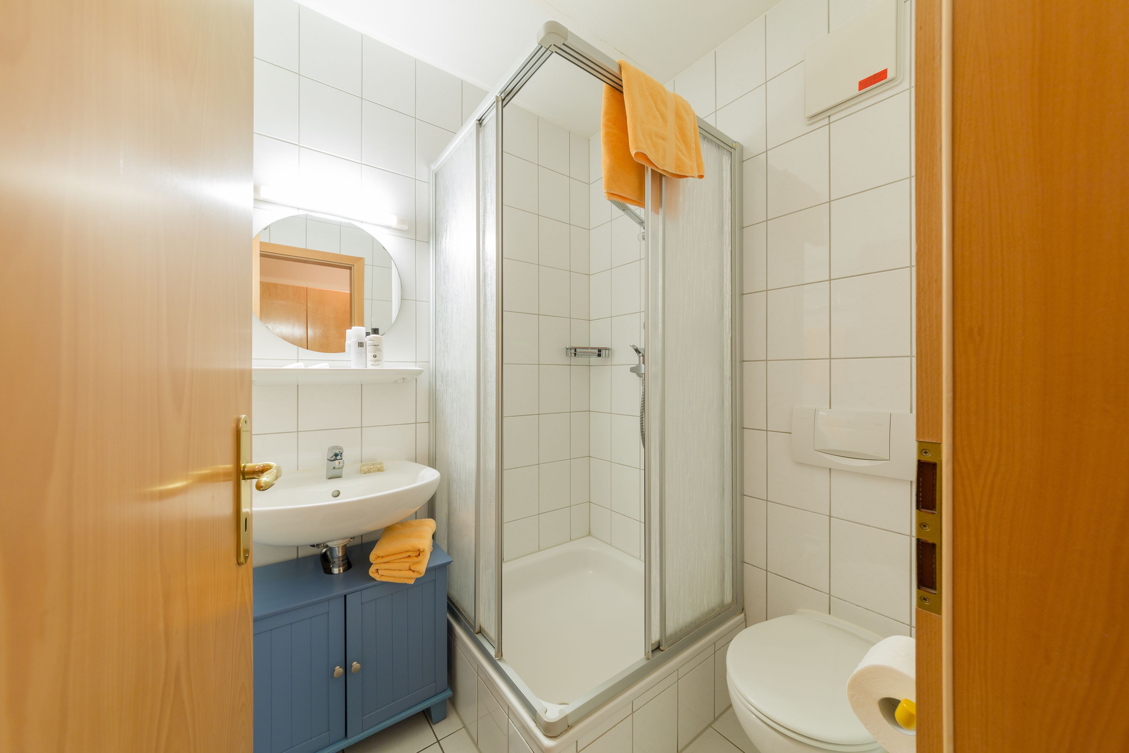 A bathroom with a shower, toilet, sink, and blue cabinet.