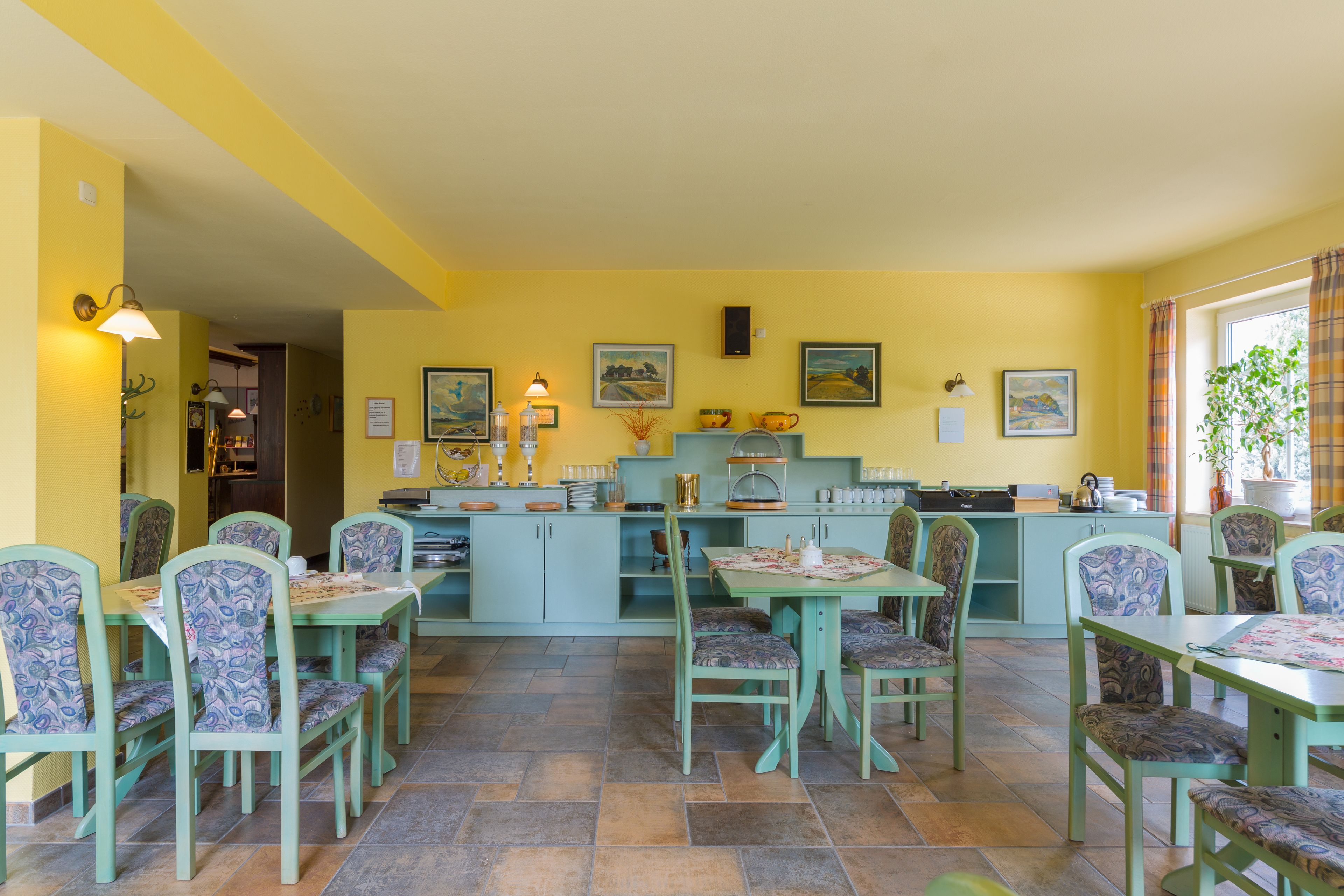 A dining area with green chairs and tables, yellow walls, and artwork on the walls.