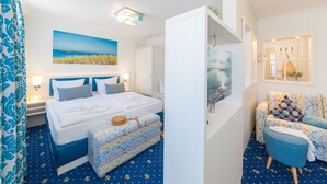 Une chambre d’hôtel avec un grand lit, un canapé, une petite table et un tableau représentant une scène de plage.